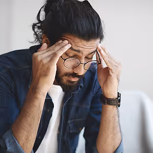 Man with glasses touching his forehead with his hands in a thoughtful pose