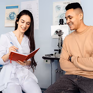 A woman doctor and a man patient smiling at each other inside a clinic