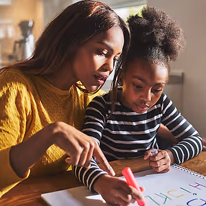 A mother and daughter are doing homework together at a table in the kitchen