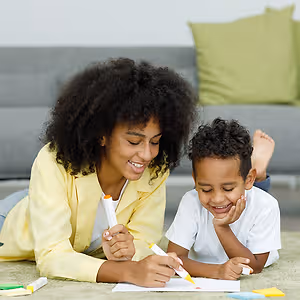 A woman and a boy lying on the floor drawing and coloring on paper with markers and crayons