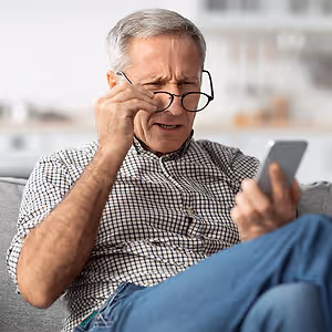 old man with glasses holding phone and squinting his eyes