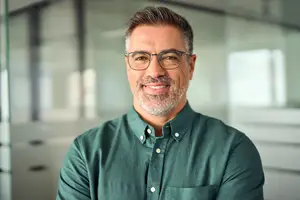A smiling man in a green shirt and glasses standing in an office