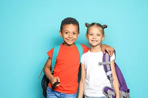 Smiling boy and girl wearing backpacks standing together against a turquoise background