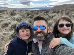 A man with his two children taking a selfie in a desert with mountains in the background