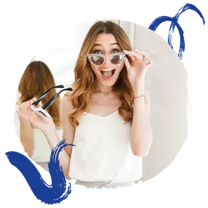A woman with brown hair is standing in front of a mirror holding a pair of sunglasses, while another woman is reflected in the mirror.