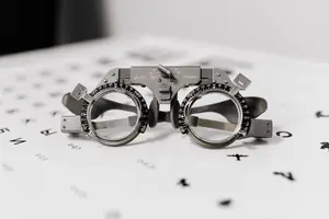 A pair of vintage-style eyeglass frames with adjustable lenses and a dial for lens strength adjustment is placed on a white chart with alphabets and numbers, likely in an optometrist's office.