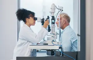 A woman in a lab coat examines a man's eyes with a medical device in a clinic setting
