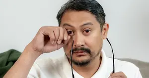 Man rubbing his eye while holding eyeglasses