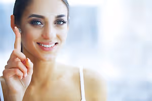 Young woman smiling and pointing to her ear with a hearing aid in it.