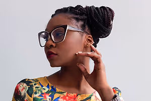 A woman with braided hair wearing glasses and a floral shirt.