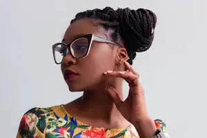 A woman with braided hair wearing glasses and a floral shirt.