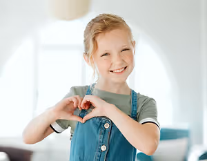 A girl smiling and forming a heart shape with her hands