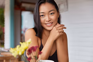 Close up of a smiling Asian woman in a black sleeveless shirt posing for a photo