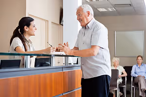 Elderly man conversing with a woman at a hospital reception counter