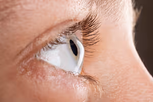 A close-up view of a person's eye, showcasing eyelashes and a teardrop in the corner of the eye.