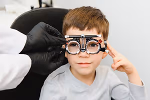 A young boy is wearing a pair of glasses and is looking at the doctor who is adjusting the glasses