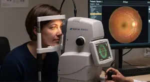 A woman is having her eyes examined by a doctor using a Topcon NW400 optical coherence tomography device, with the results displayed on a monitor in a medical setting.