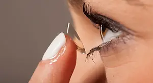 A woman inserting a clear contact lens into her eye while looking at her reflection