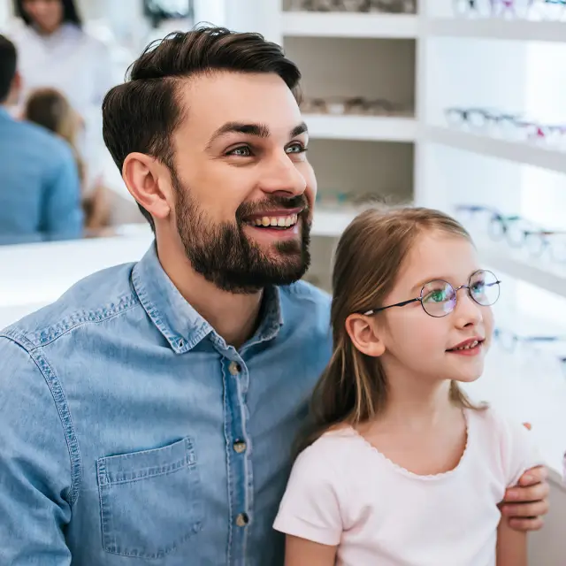 Man and a young girl in a store with glasses on a rack in the background.