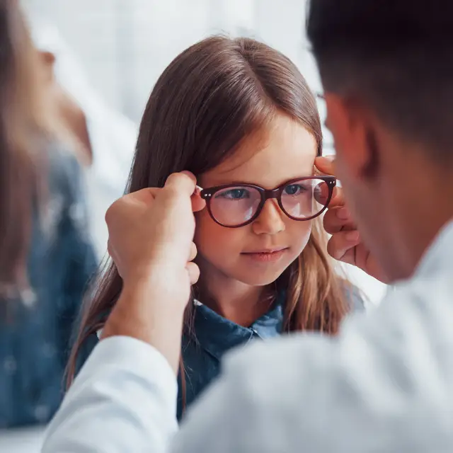 A young girl with glasses getting a checkup from an optometrist