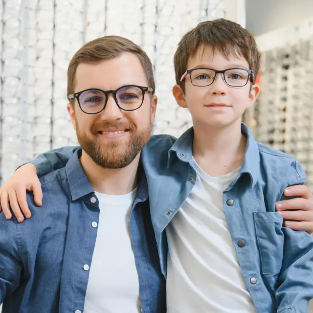 A man and a boy in glasses are standing next to each other and smiling for the camera