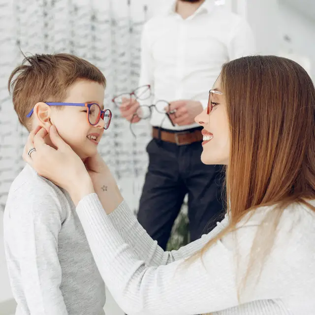 A mother helping her son put on a pair of glasses in an optical store