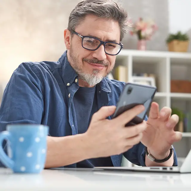Man sitting at a desk looking at his phone and smiling
