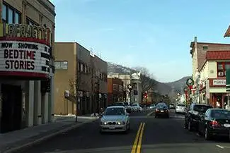 A daytime view of a street with buildings and cars driving on the road, one of the buildings has a sign that reads "Now Showing Bedtime Stories"