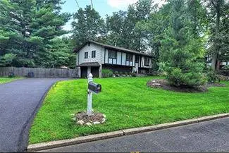 A house in the middle of a green lawn with a mailbox and trees