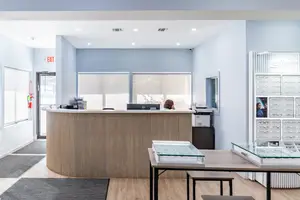 The front desk of Wesley Eye Care with a woman sitting at a computer with eyeglasses on display on the right