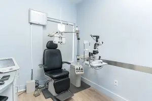 A eye doctor's office with an eye examination chair and a monitor on the wall.