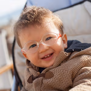 A baby with glasses and a brown coat smiles
