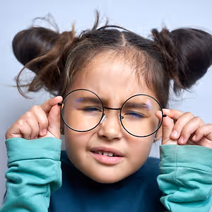 A young girl with glasses looks intently at something in front of her, with her eyes squinting slightly.