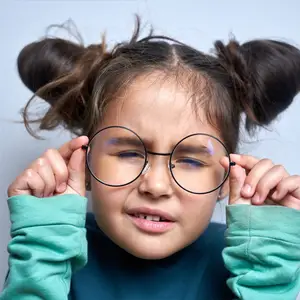 A young girl with glasses looks intently at something in front of her, with her eyes squinting slightly.