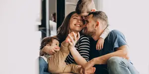 A family of four, two young boys, a mother and father are sitting on a couch and smiling