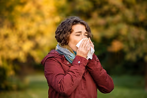 Person sneezing into a tissue outdoors