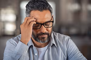 Man wearing glasses rubbing his temple with a concerned expression