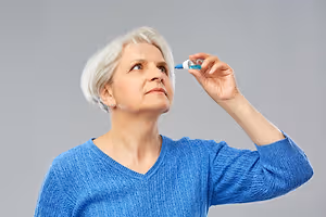 Older woman holding an eye drop bottle near her eye