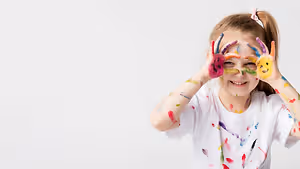 Little girl with paint on her hands and face smiling at the camera