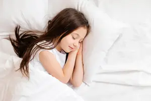 A young girl sleeping in a bed with white sheets and pillows