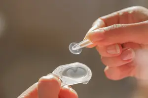A person holding a transparent glass object and a glass tube with a dropper tip, possibly inserting a contact lens.