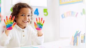 Little girl showing her rainbow-colored painted hands at a table in a Gray TN eye care clinic.
