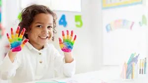 Little girl showing her rainbow-colored painted hands at a table in a Gray TN eye care clinic.