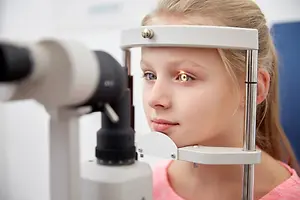 A young girl is undergoing an eye examination with an ophthalmoscope.