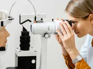 A woman is examining a patient's eyes with an ophthalmoscope.