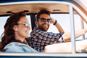 A couple is smiling while driving a car on a sunny day