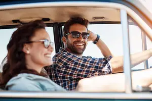 A couple is smiling while driving a car on a sunny day