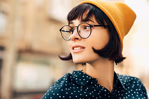 A Stockbridge woman with short hair and bangs wearing glasses and a yellow beanie with a polka-dot shirt