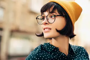 A Stockbridge woman with short hair and bangs wearing glasses and a yellow beanie with a polka-dot shirt