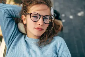 Woman wearing glasses sitting outside on a bench with her head resting on her arm